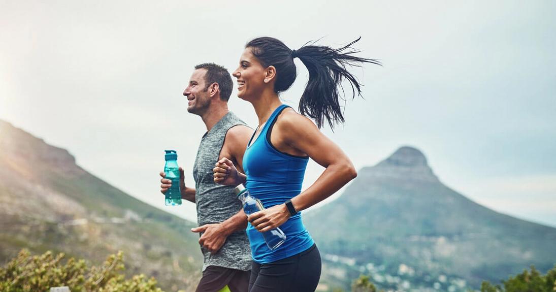 Couple each holding water bottles jogging outdoors